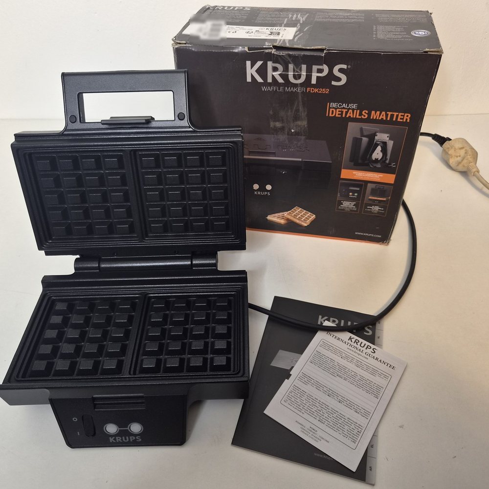 Das Waffeleisen aufgeklappt, dahinter der Originalkarton „Waffle Maker FDK252“, davor Anleitung und Garantie-Faltblatt.
