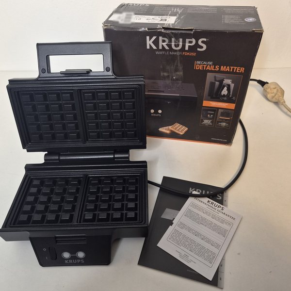 Das Waffeleisen aufgeklappt, dahinter der Originalkarton „Waffle Maker FDK252“, davor Anleitung und Garantie-Faltblatt.