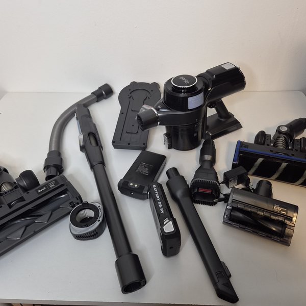 Alle Teile ausgelegt: Handteil, Knickrohr, Bodendüse, Hartbodendüse, Mini-Turbobürste, zwei Akkus, Ladegerät, Verlängerungsschlauch, Fugendüse, 2-in-1-Bürste, Filter und Wandhalterung.