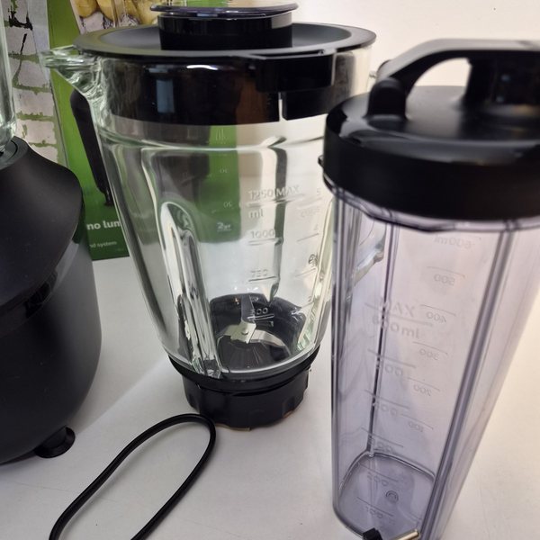 Ein Glasbehälter mit Deckel und Messbecher, daneben eine To-Go-Flasche mit Trinkdeckel.