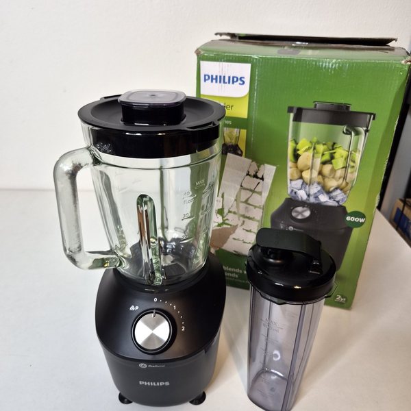 Motoreinheit mit aufgesetztem Glasbehälter und eine To-Go-Flasche vor dem Originalkarton.